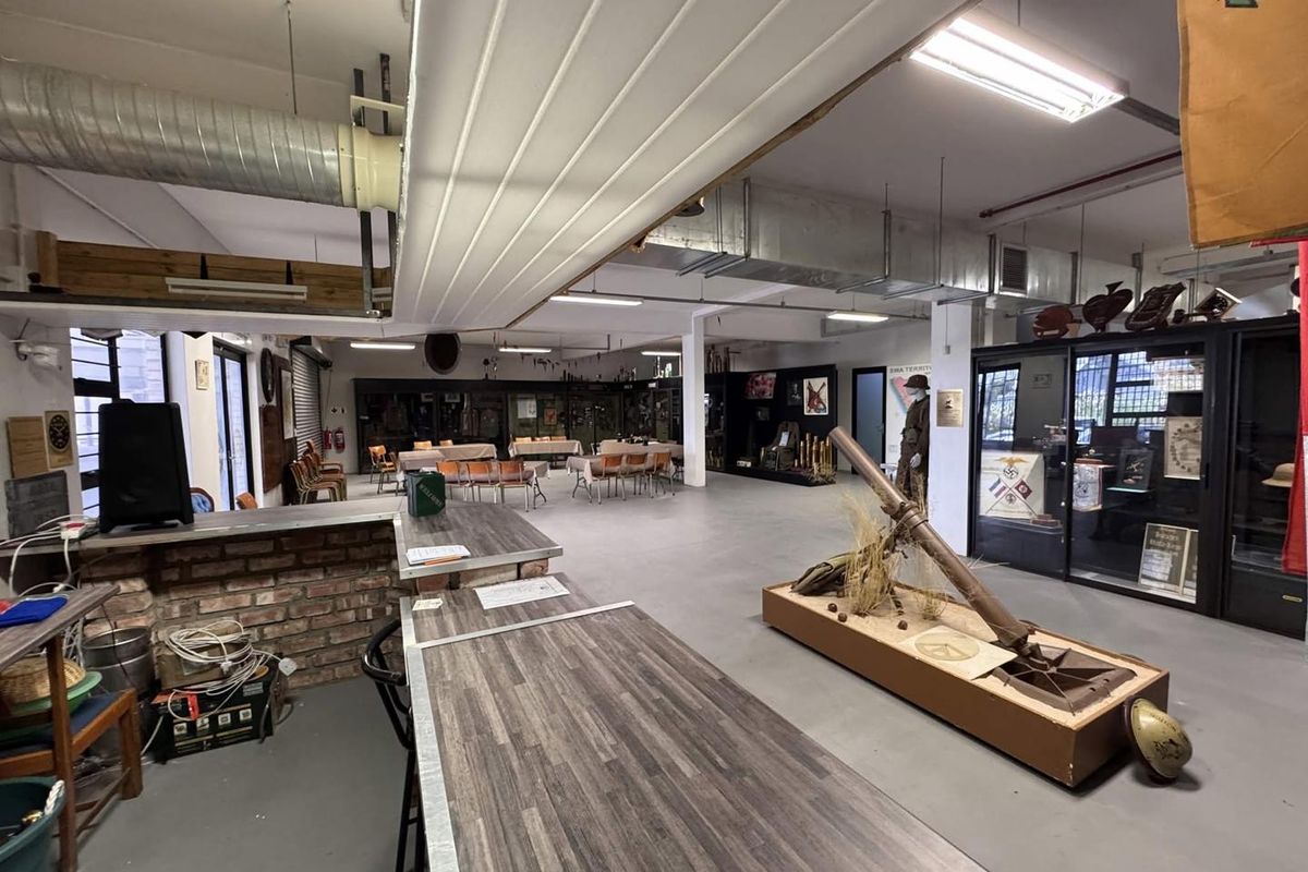 Spacious clubhouse interior featuring industrial-style exposed ducting, concrete flooring, a brick-faced bar counter, and integrated display cabinets for historical exhibits.