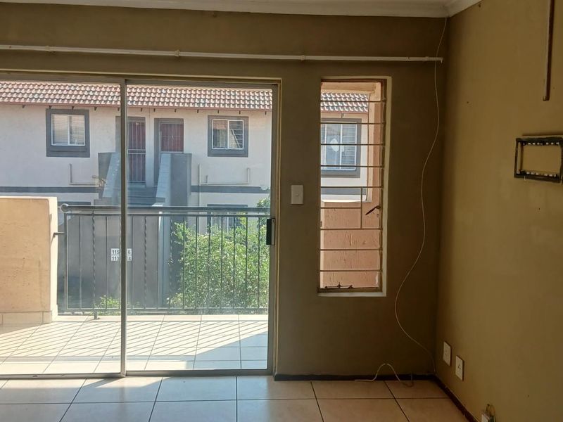 An empty living room featuring tiled flooring and a sliding glass door providing access to a balcony with security bars.