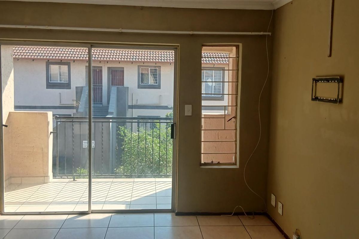 An empty living room featuring tiled flooring and a sliding glass door providing access to a balcony with security bars.