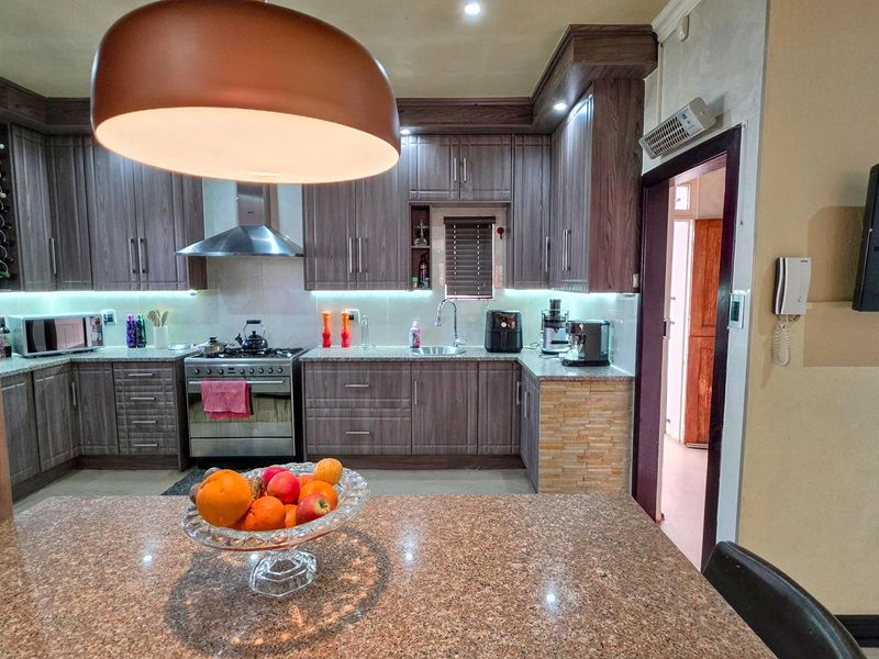 A well-appointed kitchen featuring dark wood cabinetry, granite countertops, stainless steel appliances, and modern under-cabinet lighting, providing a functional and stylish cooking space.