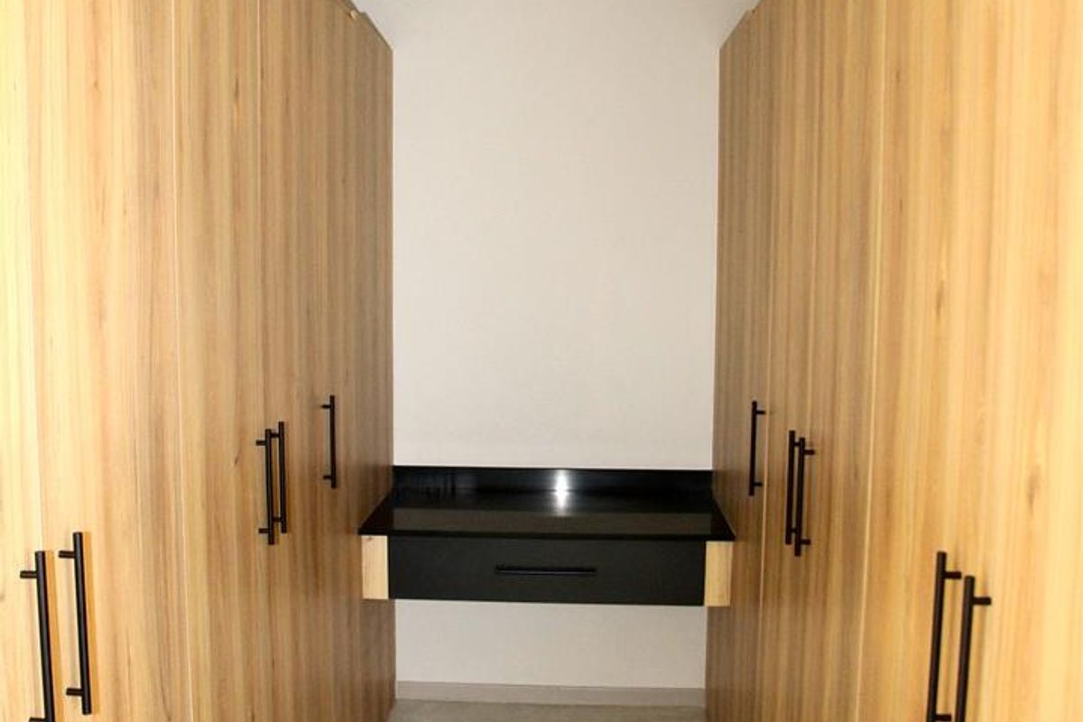 A modern walk-in closet featuring floor-to-ceiling light wood cabinetry with black hardware and a built-in vanity desk with a black countertop.