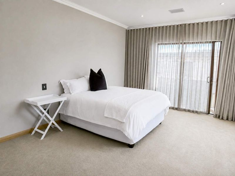 A well-maintained bedroom featuring neutral carpeting, recessed lighting, and a large sliding glass door with floor-to-ceiling curtains providing natural light.