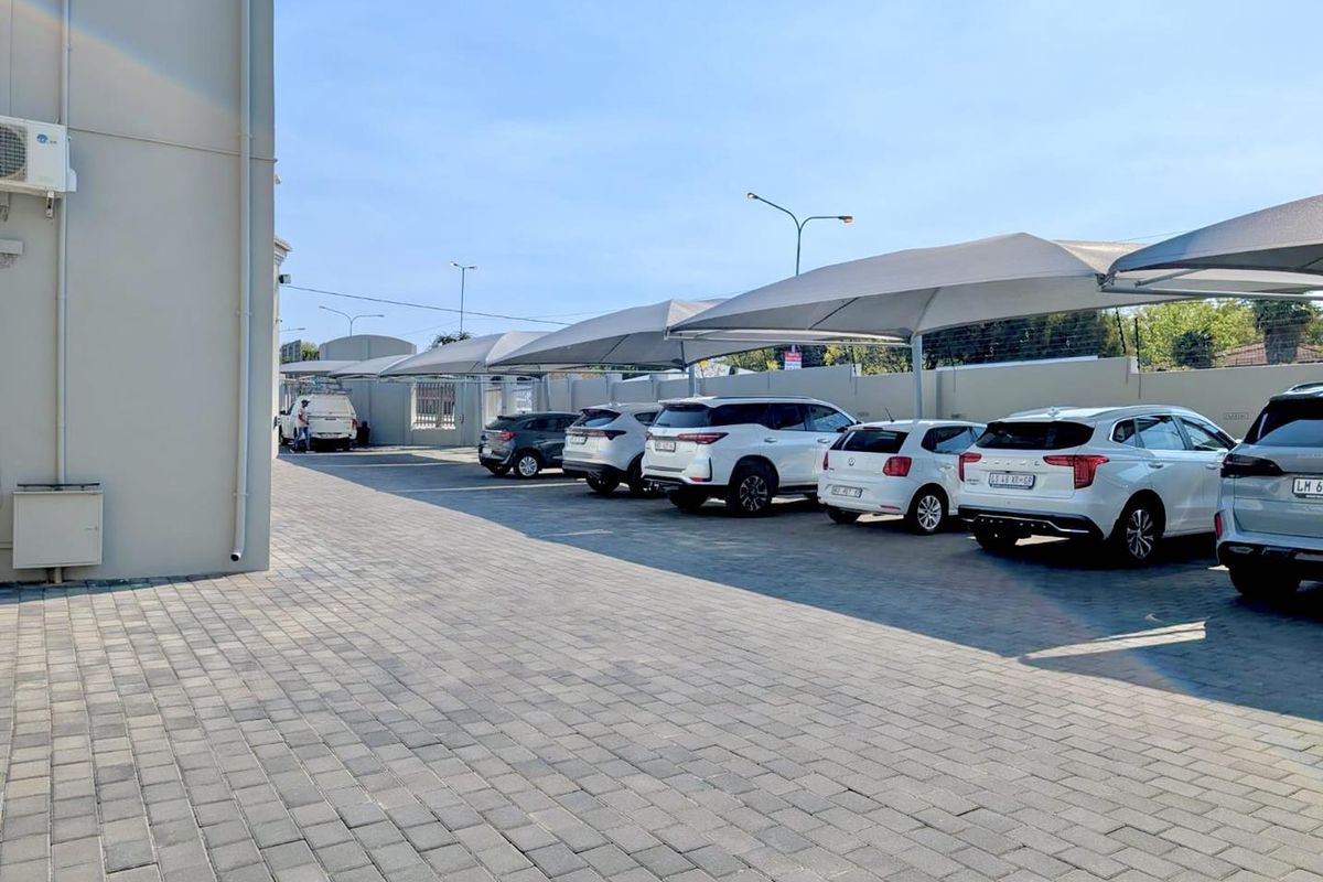 A well-maintained paved parking area featuring multiple shade cloth carports and secure perimeter walling.
