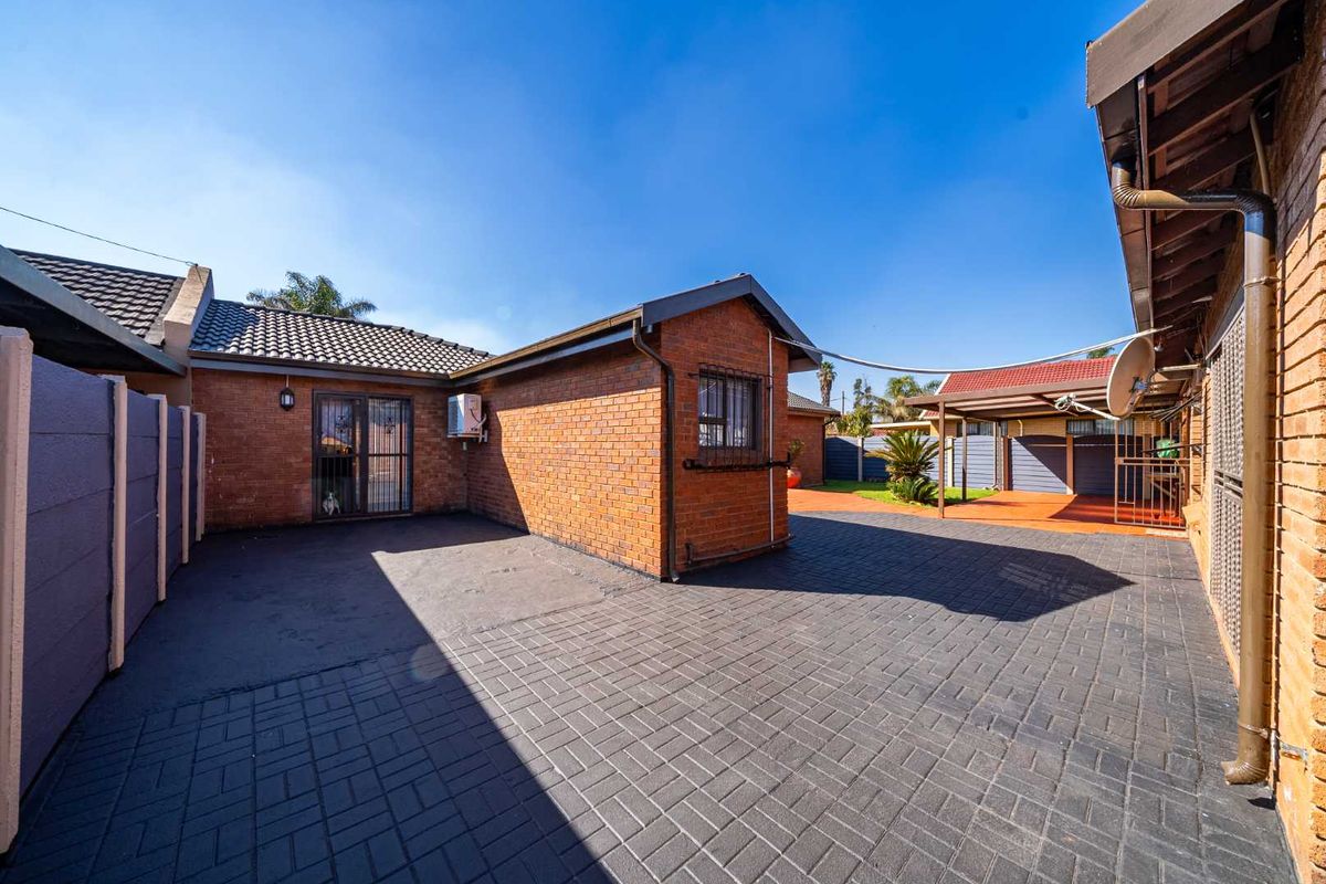 A well-maintained rear exterior area featuring paved courtyard space, brick facade, and a covered patio structure.