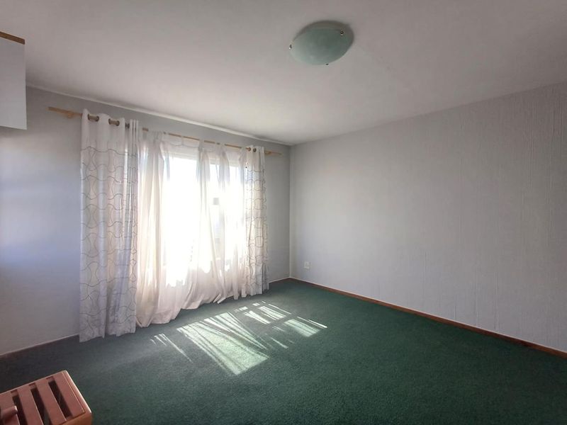 A vacant bedroom featuring green carpet flooring, a central ceiling light fixture, and a large window with curtain rod.