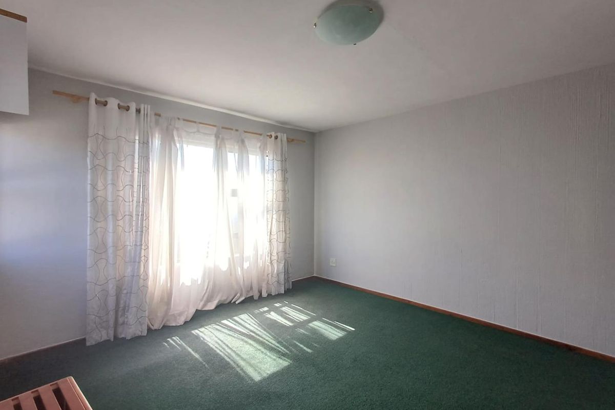A vacant bedroom featuring green carpet flooring, a central ceiling light fixture, and a large window with curtain rod.