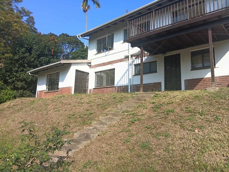 Rear view of a two-story house featuring a timber balcony, brick and plaster facade, and concrete stairs leading to the garden area.