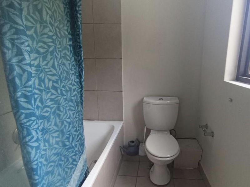 A functional bathroom featuring a bathtub with a shower curtain, a standard toilet, and neutral wall and floor tiling.