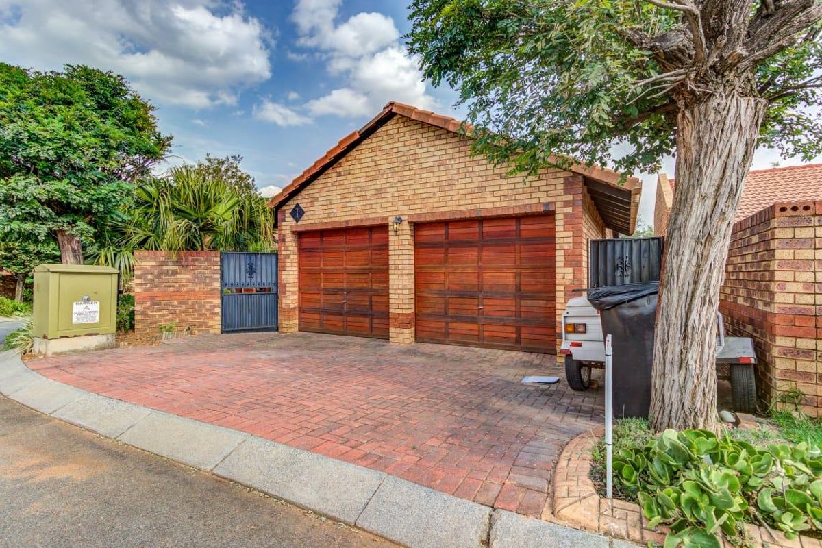 A double garage with wooden doors and a paved driveway, featuring a brick exterior and secure boundary walling.
