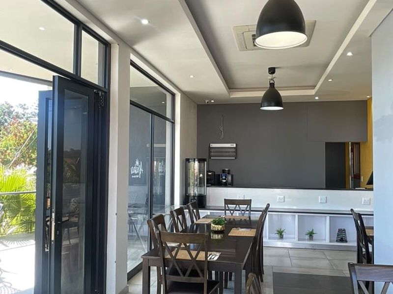 Modern open-plan dining area featuring tiled floors, recessed and pendant lighting, and large glass doors opening to an outdoor space.