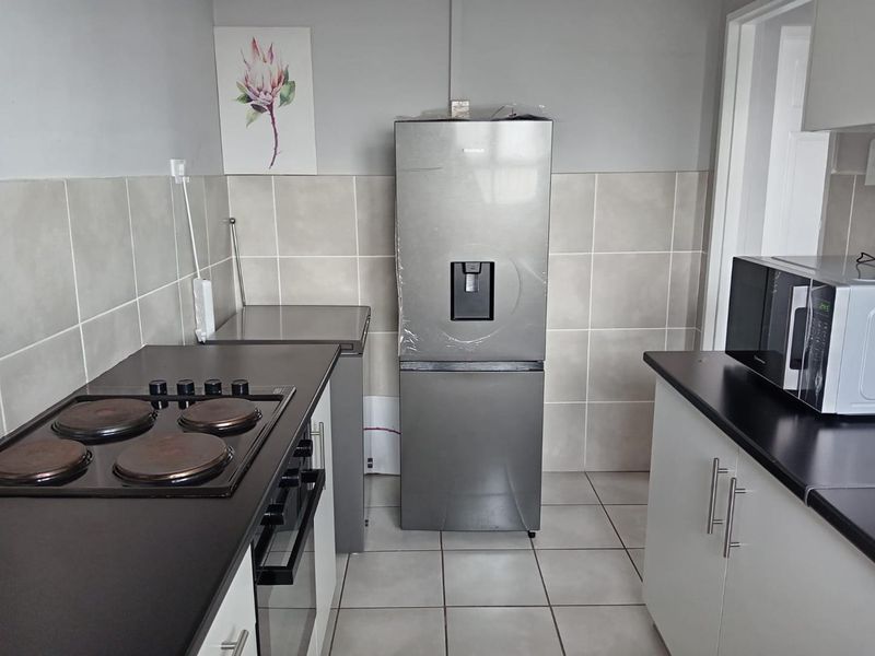A functional kitchen featuring built-in cabinetry, dark laminate countertops, an electric hob, oven, and neutral tiled splashbacks and flooring.