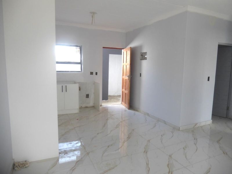 An empty kitchen area featuring marble-look floor tiles, base cabinetry, and a window, currently in an unfinished state awaiting completion.