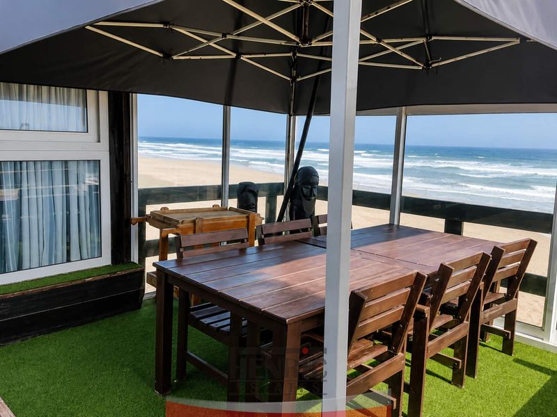Covered balcony featuring artificial grass flooring and glass balustrades, offering direct, unobstructed views of the ocean and beach.
