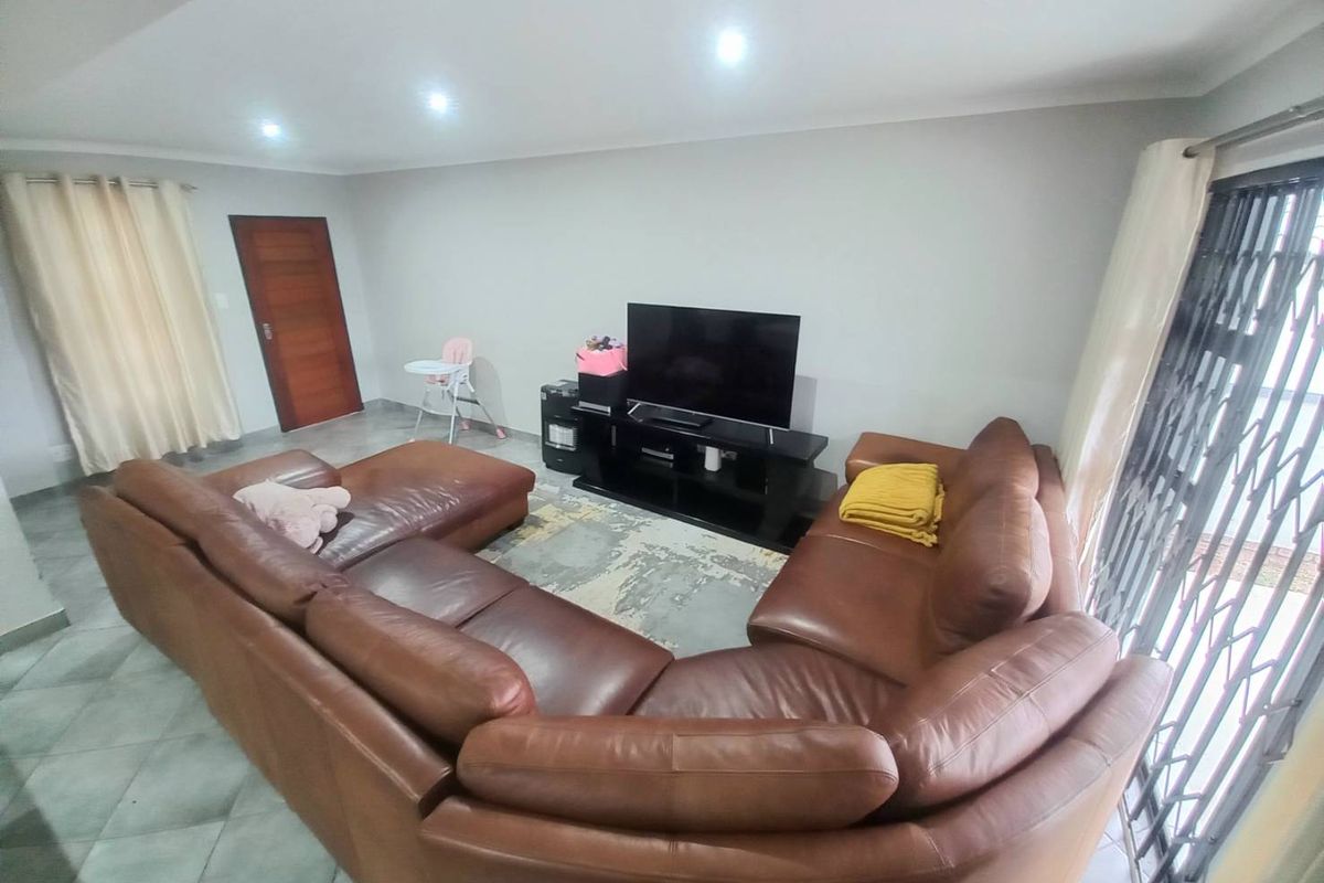 A spacious living room featuring tiled flooring, recessed downlighting, and a security gate on the sliding door leading to the exterior.
