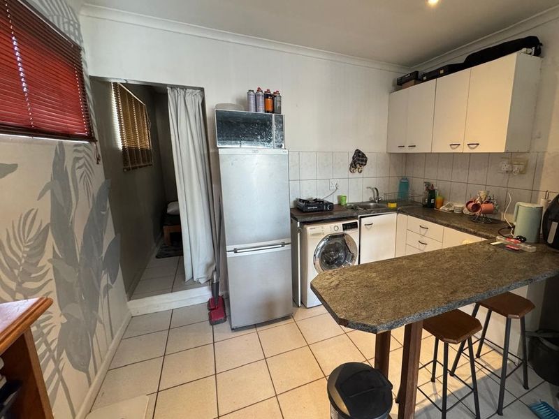 Compact kitchen featuring built-in cabinetry, a breakfast bar, tiled flooring, and integrated laundry facilities, offering a functional layout with potential for modern updates.