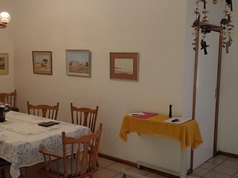 A dining room featuring tiled flooring and a central chandelier, with an open doorway leading to an adjacent living area.