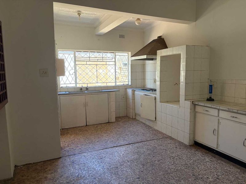 A dated kitchen featuring tiled countertops, built-in cabinetry, a double sink, and an extractor fan, offering significant potential for modernization and renovation.