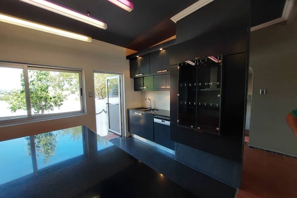 Modern kitchen featuring sleek black cabinetry, a large dark stone island, integrated dishwasher, and direct access to the outdoor area.