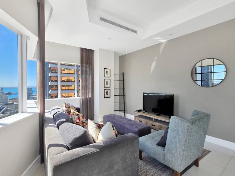 A bright and modern living room featuring large floor-to-ceiling windows with city and ocean views, recessed ceiling lighting, and ducted air conditioning.