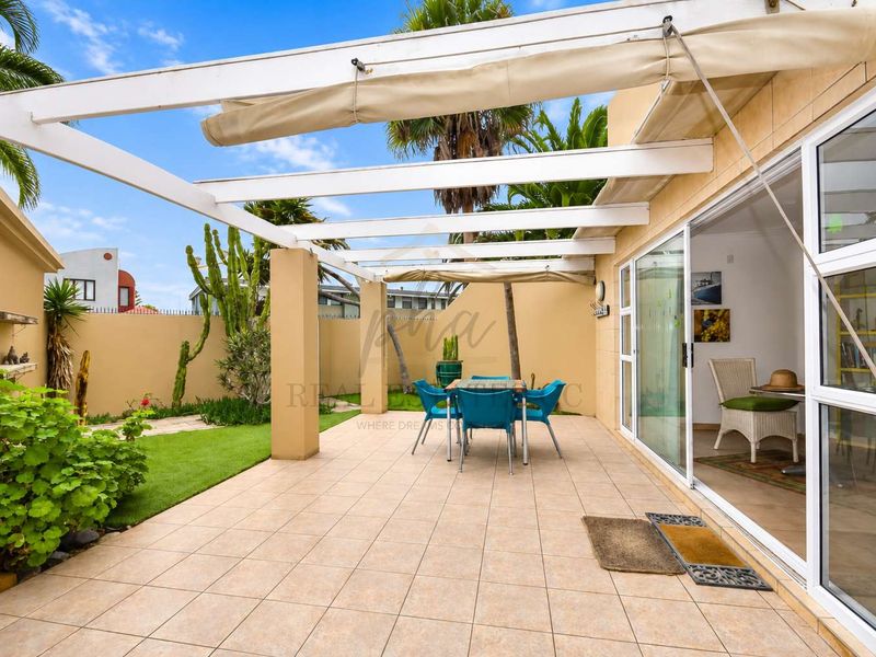 A well-maintained outdoor patio featuring tiled flooring, a pergola structure with a retractable awning, and direct access to the interior through sliding glass doors.