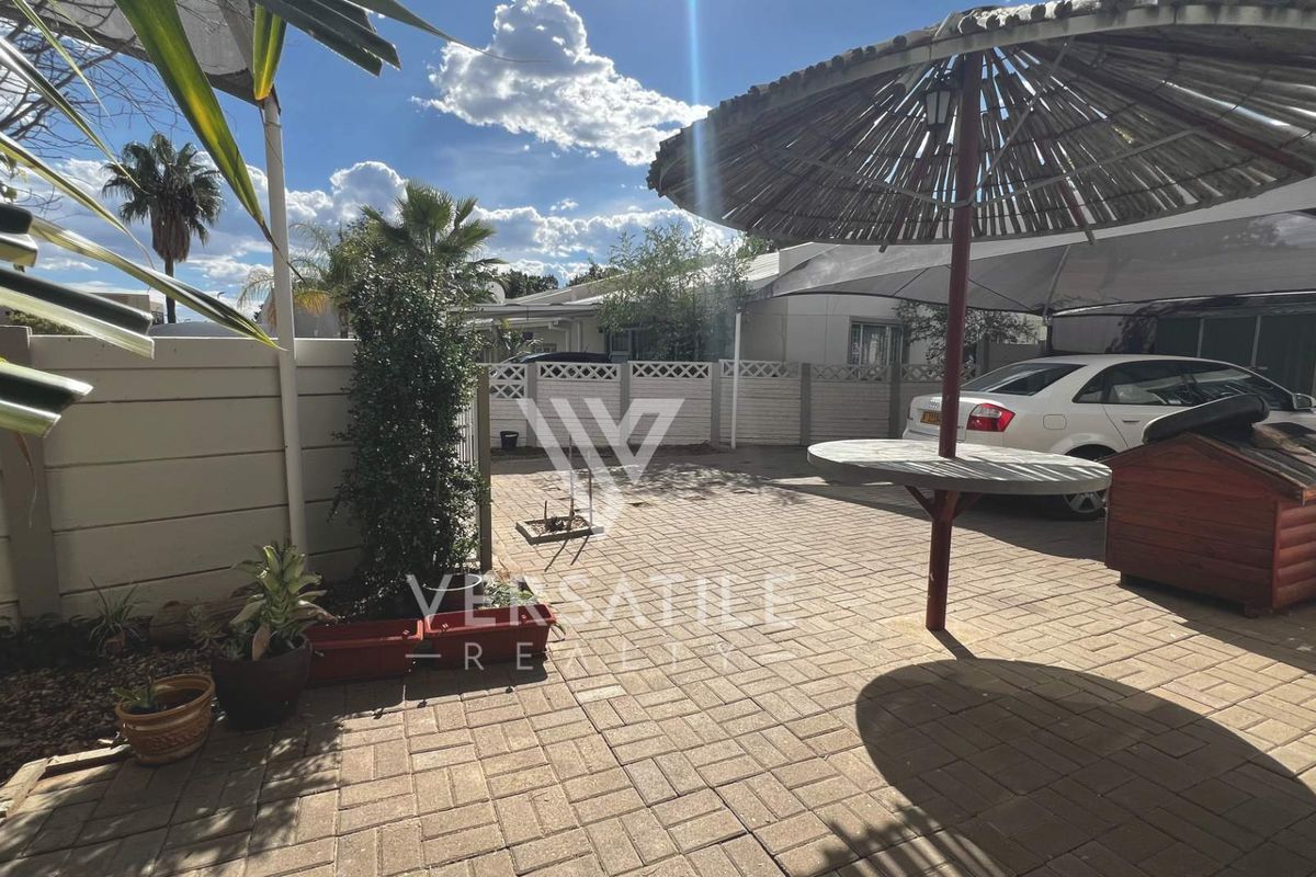 A paved outdoor courtyard area featuring a perimeter boundary wall and a fixed central umbrella structure, suitable for parking or outdoor entertainment.