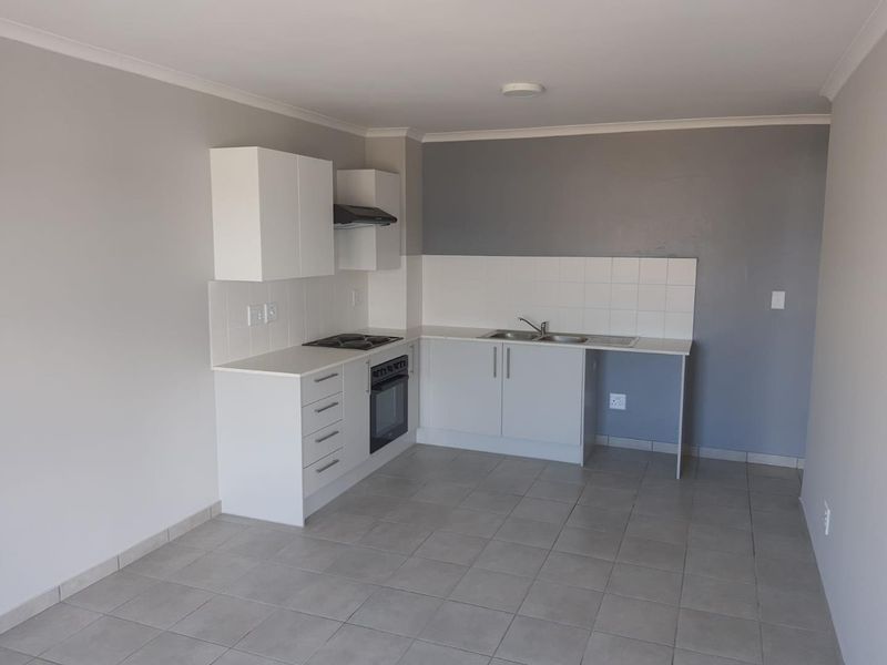 A clean, functional kitchen featuring white cabinetry, built-in oven and hob, tiled backsplash, and neutral tiled flooring in an open-plan layout.