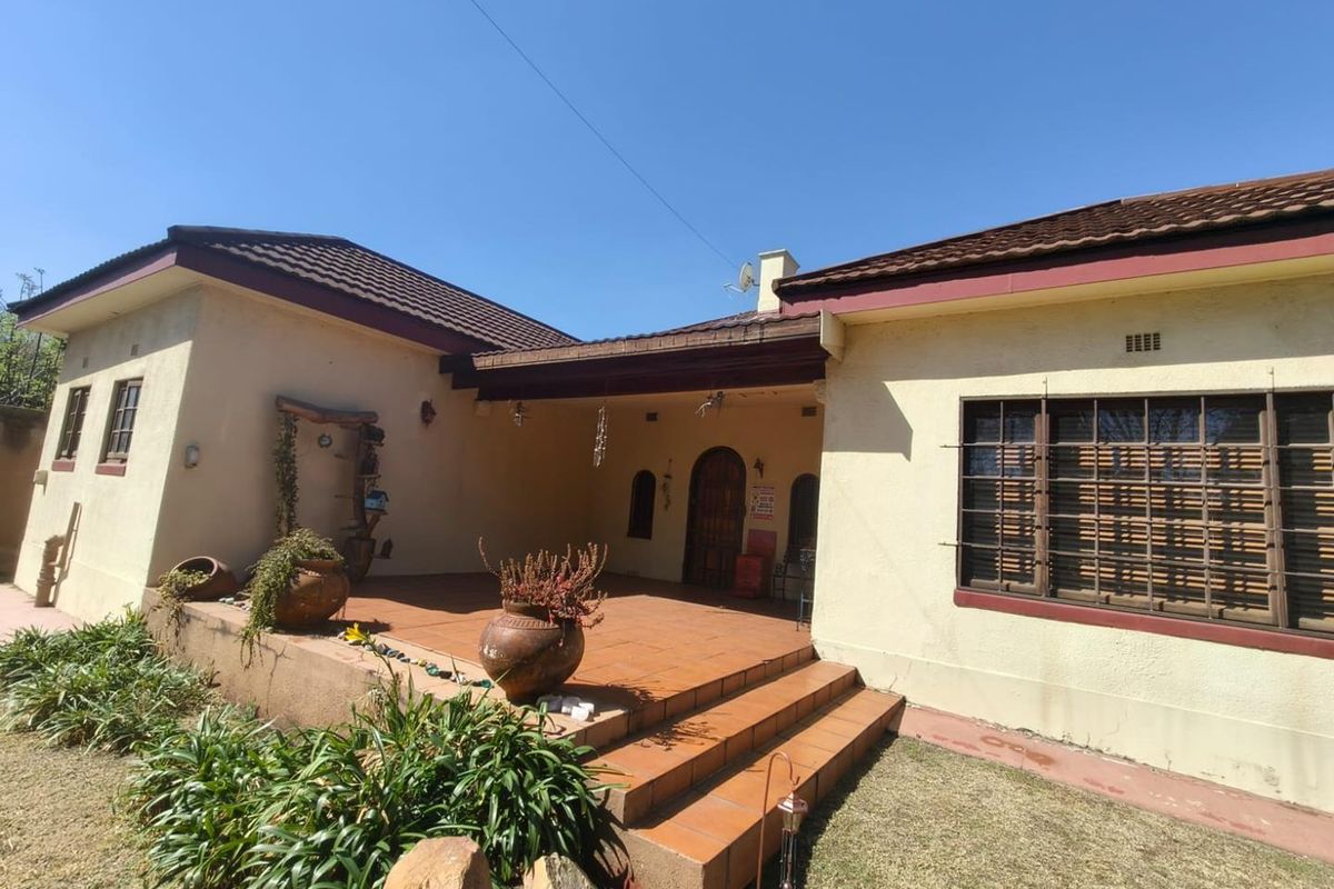 A rear view of the house featuring a covered tiled patio, terracotta steps, and security bars on the windows.