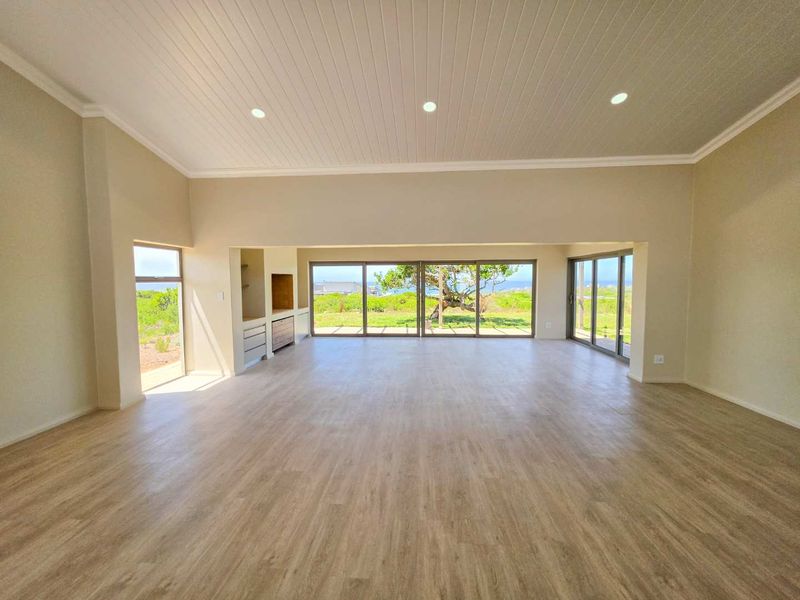 Spacious open-plan living area featuring light laminate flooring, recessed lighting, tongue and groove ceiling, and large sliding glass doors with scenic coastal views.