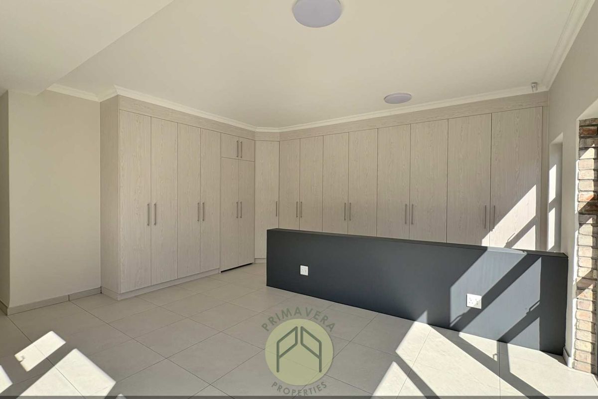 A spacious, modern bedroom featuring extensive built-in cabinetry, neutral tiled flooring, and large windows allowing for ample natural light.