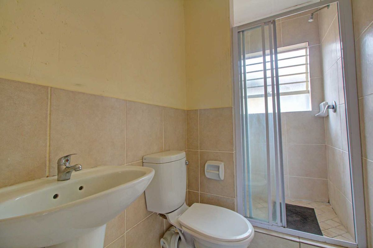 A functional bathroom featuring a pedestal basin, toilet, and a glass-enclosed shower with tiled walls.
