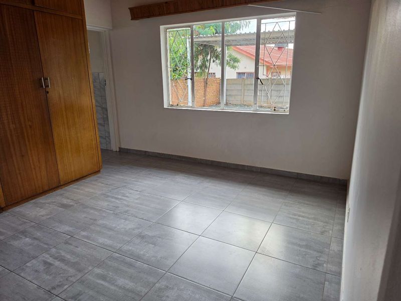 A vacant bedroom featuring tiled flooring and a built-in wooden wardrobe, offering a clean and neutral space ready for personalization.
