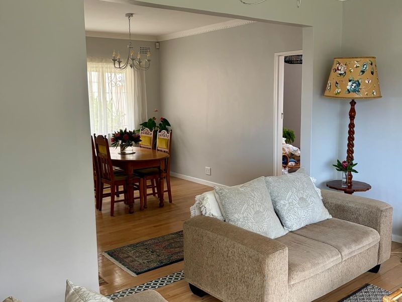 An open-plan living and dining area featuring hardwood flooring, crown molding, and a classic chandelier, creating a bright and connected living space.