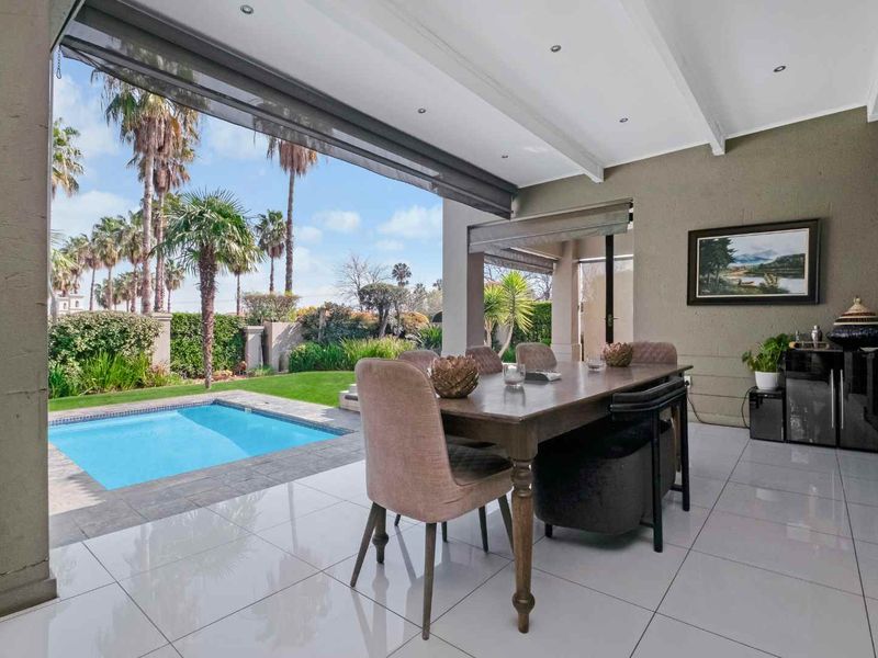 A spacious covered patio featuring tiled flooring and recessed lighting, seamlessly flowing out to a private swimming pool and well-maintained garden area.
