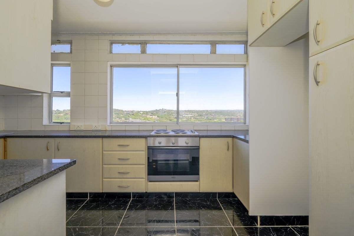 A functional kitchen featuring built-in cabinetry, granite countertops, an integrated oven and hob, and large windows offering natural light and scenic views.