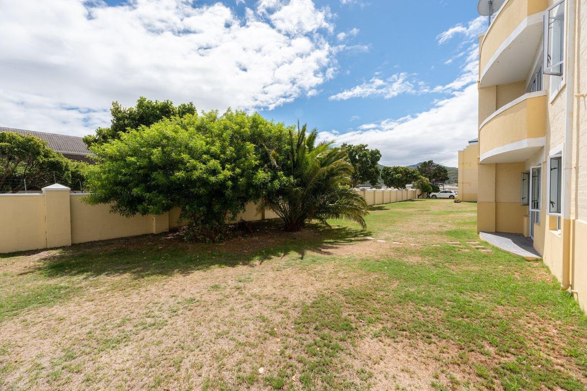 A view of the communal garden area adjacent to the apartment building, featuring established trees and a perimeter boundary wall.