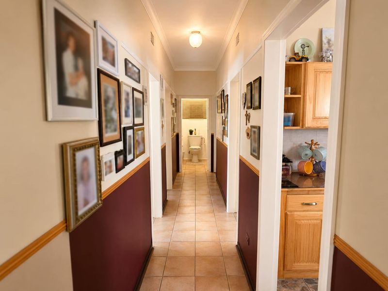 A well-lit hallway featuring tiled flooring, dado rails, and coving, providing access to multiple rooms including a bathroom at the end.