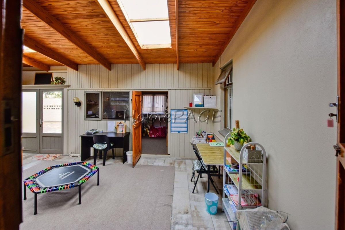 Spacious living area featuring a high exposed timber beam ceiling with a skylight, timber wall paneling, and access through french doors.