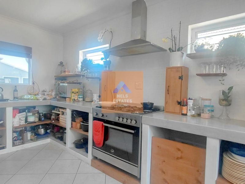 A functional kitchen featuring concrete countertops, open shelving, and stainless steel appliances including a gas hob and extractor fan.