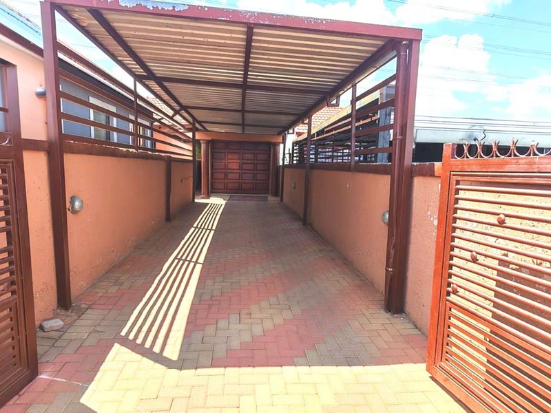 A secure driveway featuring a covered carport, paved flooring, and gated entrance leading to a garage.