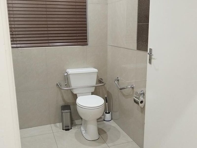A clean, modern accessible bathroom featuring neutral floor-to-ceiling tiling, stainless steel grab rails, and a white toilet suite.