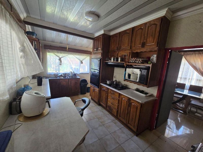 A functional kitchen featuring traditional wooden cabinetry, built-in appliances, and tiled flooring, offering a classic layout with potential for modern updates.