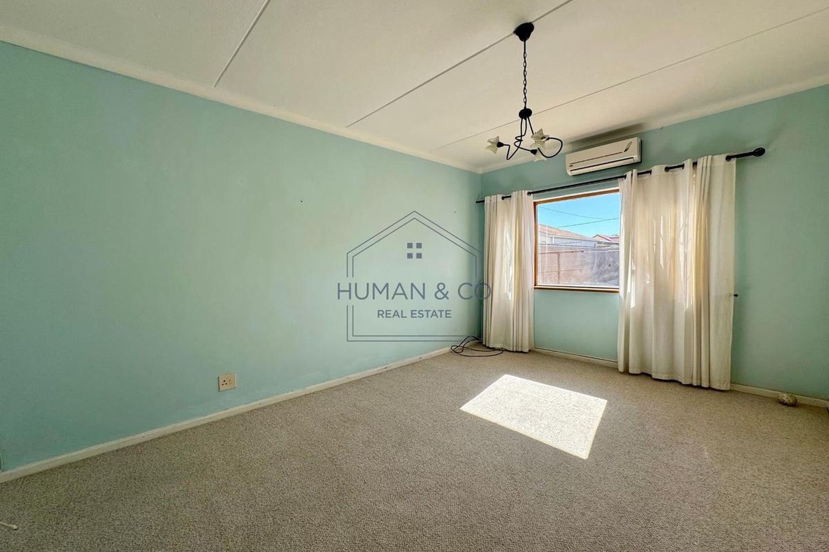 A bright, empty bedroom featuring neutral carpeting, a wall-mounted air conditioning unit, and a central light fixture.