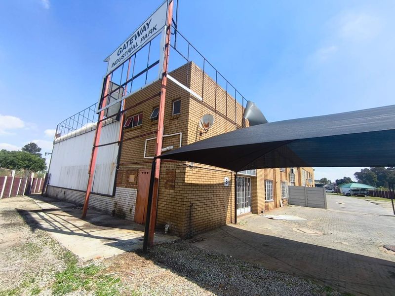 Exterior view of an industrial unit at Gateway Industrial Park, featuring brick construction, a paved driveway, and a shade cloth carport structure.