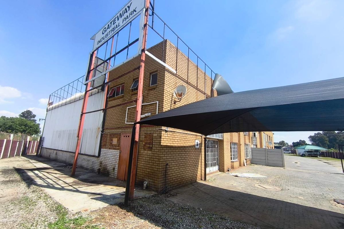 Exterior view of an industrial unit at Gateway Industrial Park, featuring brick construction, a paved driveway, and a shade cloth carport structure.