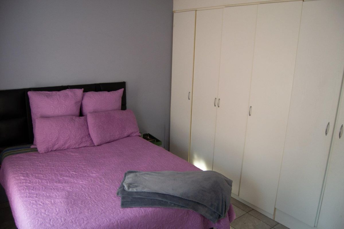 A bedroom featuring built-in floor-to-ceiling wardrobes with white cabinetry and tiled flooring.