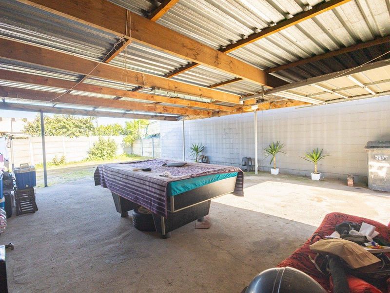 A covered outdoor patio area featuring a corrugated metal roof, exposed timber rafters, and concrete flooring, suitable for renovation or outdoor entertainment space.