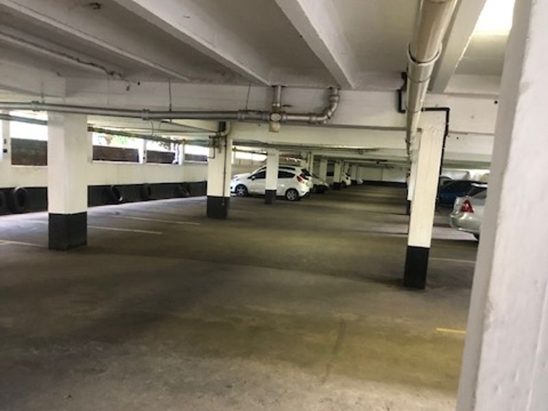 A functional covered parking garage area featuring concrete structural pillars and exposed overhead plumbing.