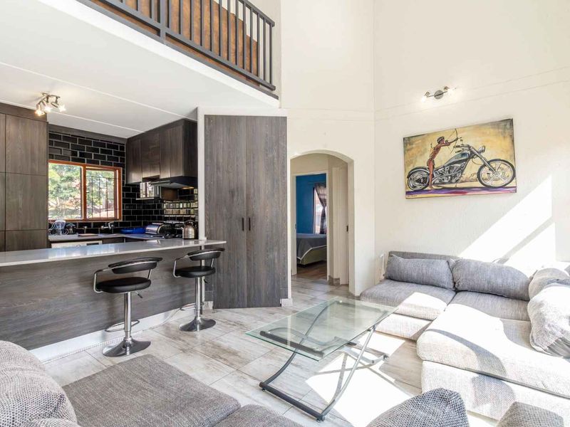 Open-plan living area featuring a modern kitchen with breakfast bar, tiled flooring, and a mezzanine level with a metal balustrade.