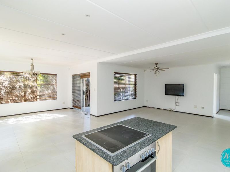 Spacious open-plan living area featuring a central kitchen island with built-in oven and cooktop, tiled flooring, and sliding door access to the exterior.