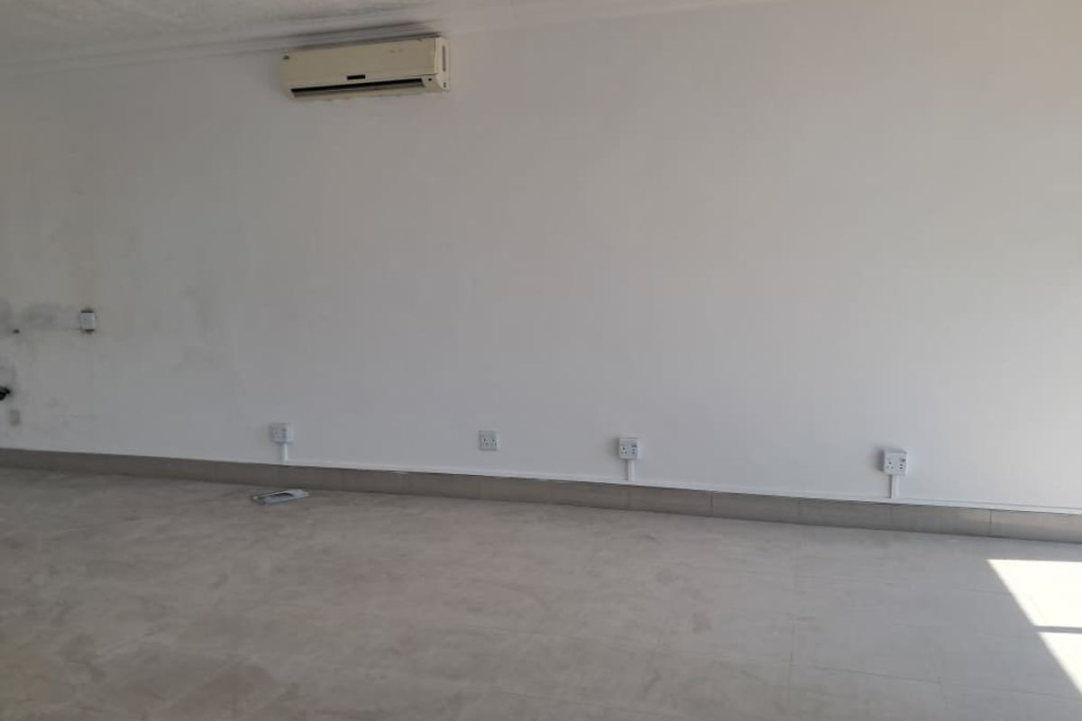 An empty, open-plan retail space featuring tiled flooring, wall-mounted air conditioning, and multiple electrical outlets, ready for custom fit-out.